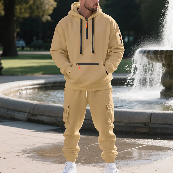 Man wearing a beige tracksuit standing in front of a fountain