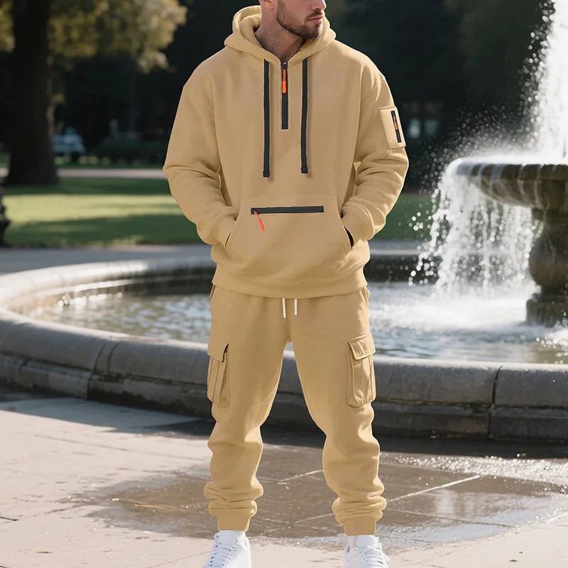 Man wearing a beige tracksuit standing in front of a fountain