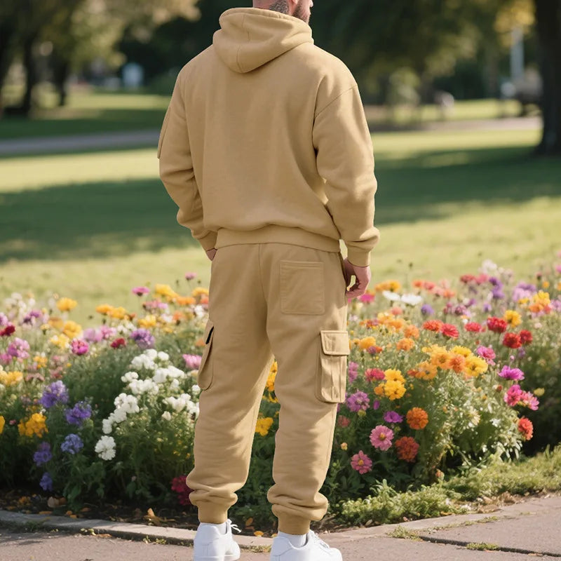 Person wearing a beige tracksuit standing in a park with colorful flowers.
