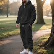 Man wearing a black hoodie and cargo pants standing on a path in a park.