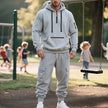 Man in a gray tracksuit standing on a playground with children playing in the background