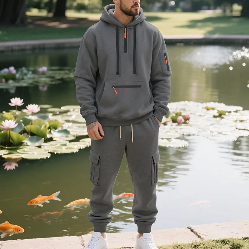 Person wearing a gray hoodie and pants standing by a pond with lilies and fish.