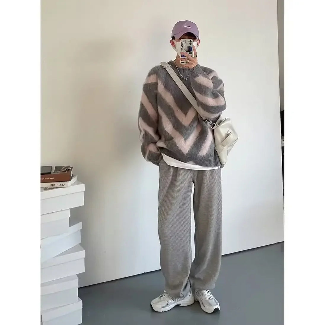 Person wearing a striped sweater and gray pants in a minimal indoor setting.