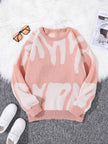 Pink sweater with white abstract patterns on a gray surface with white sneakers and sunglasses.