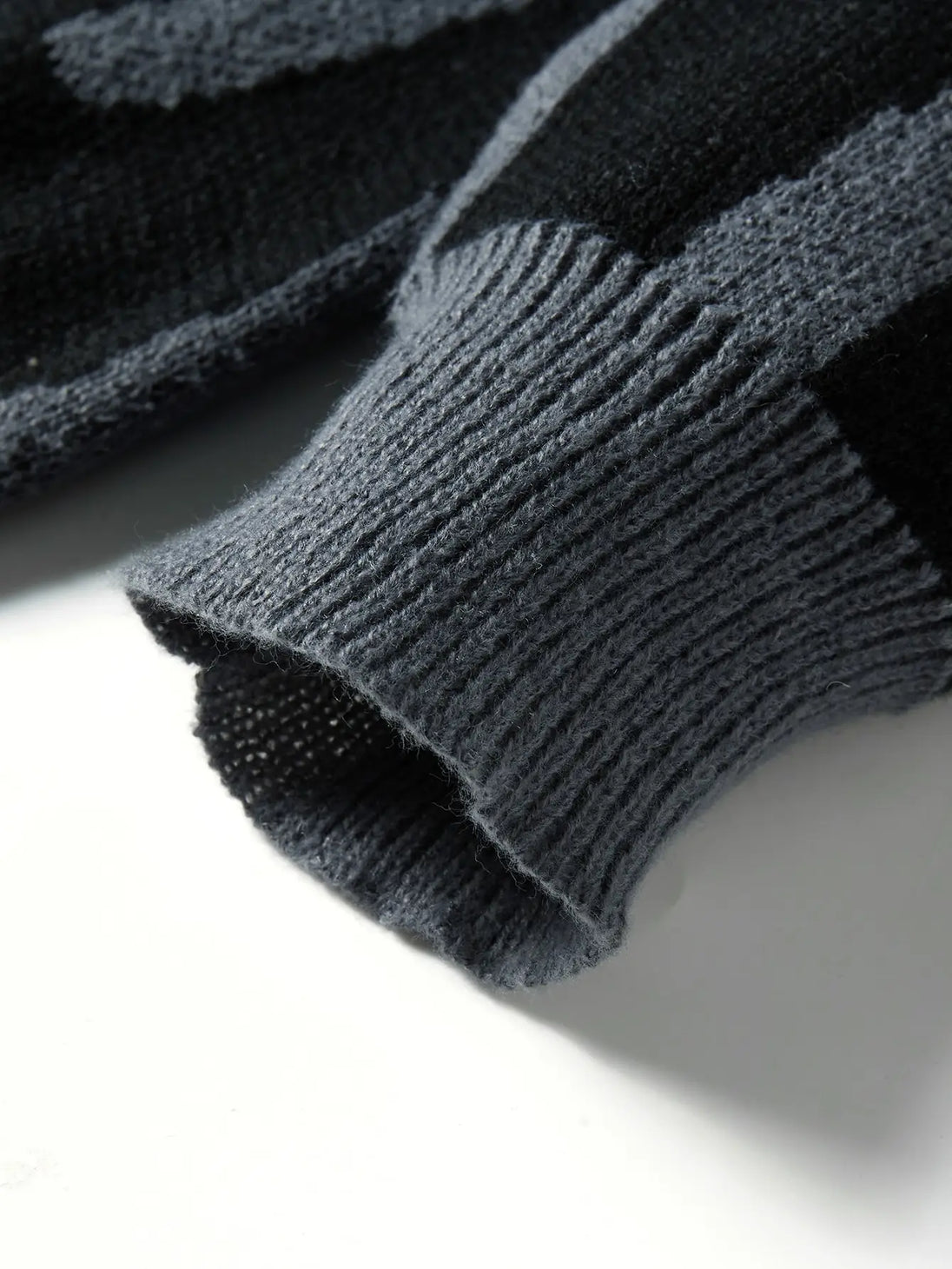 Close-up of a dark gray knitted sweater sleeve on a light background