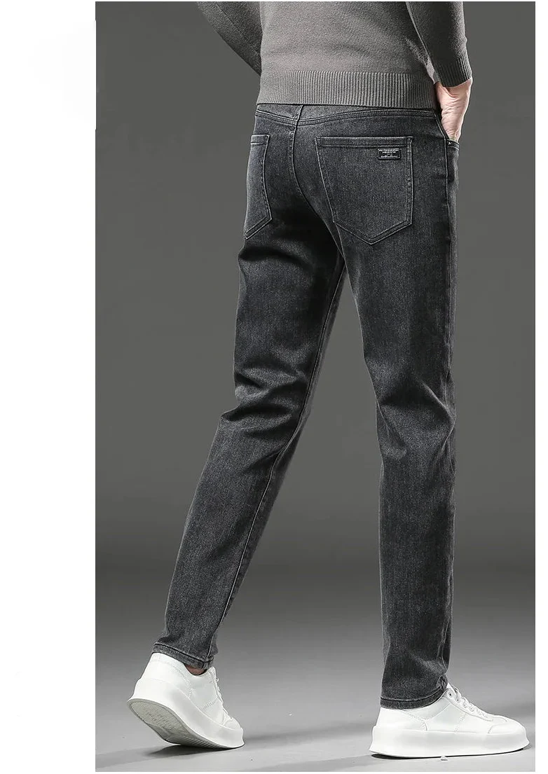 Person wearing dark gray jeans and white sneakers on a gray background