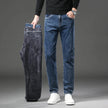 Person holding a pair of dark gray jeans next to a pair of blue jeans on a gray background