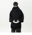 Person wearing a black oversized hoodie holding white headphones on a white background