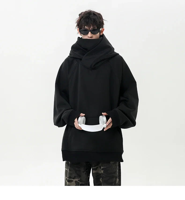 Person wearing a black oversized hoodie holding white headphones on a white background