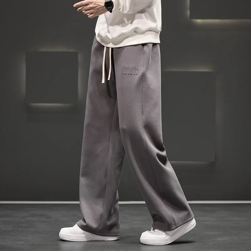 Person wearing gray sweatpants with a brand logo on a dark background