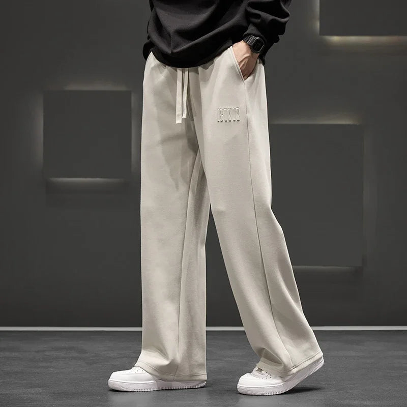 Person wearing light gray sweatpants with a brand logo on a dark background