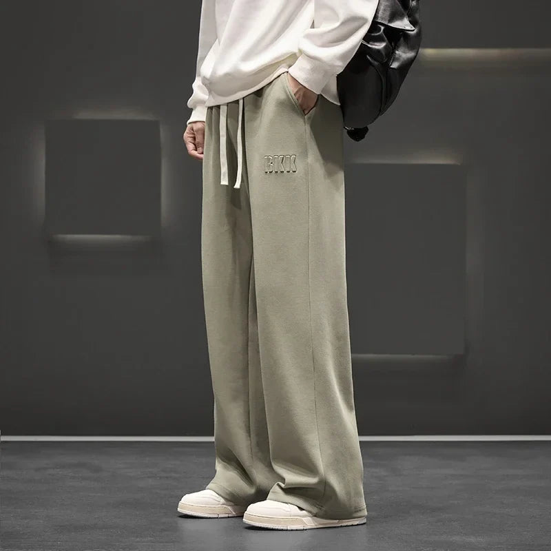 Person wearing light green sweatpants with a logo, standing against a dark background