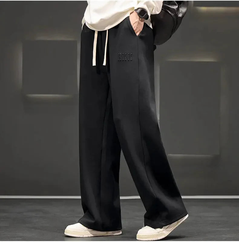 Person wearing black wide-leg pants with a brand logo, standing against a gray background.