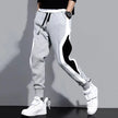 Gray jogger pants with black and white stripe worn by a person on a gray background
