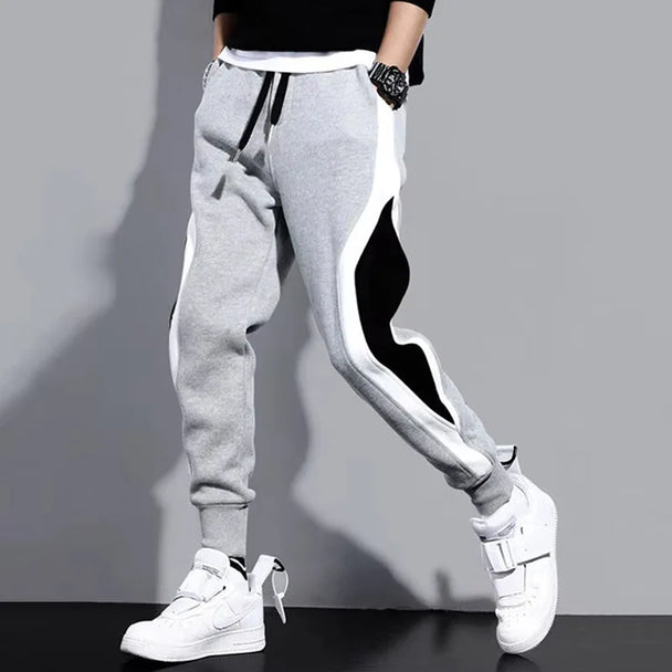 Gray jogger pants with black and white stripe worn by a person on a gray background