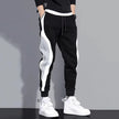 Black jogger pants with white stripes worn by a person on a gray background