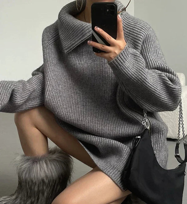Person wearing a gray oversized sweater with a black handbag, sitting on a gray surface.