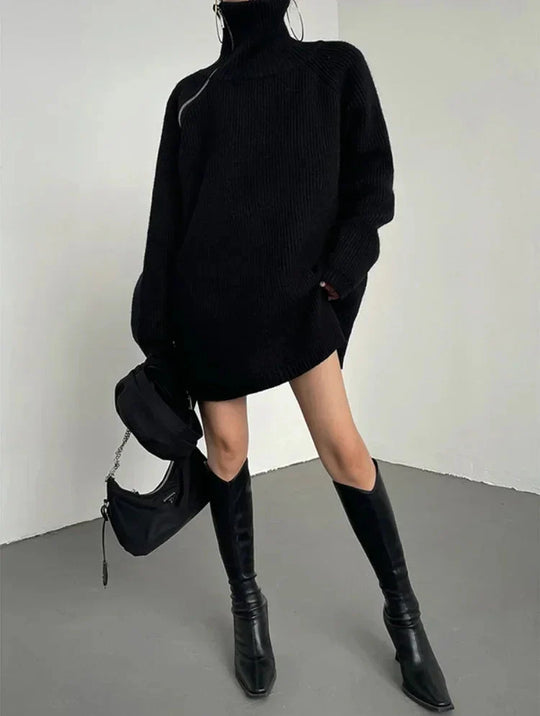 Person wearing a black oversized sweater and knee-high boots against a plain background