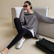 Woman sitting on a couch wearing a gray sweater and black leggings with a black handbag beside her.