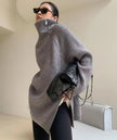 Person wearing a gray oversized sweater and sunglasses indoors.