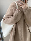 Person wearing a beige knitted sweater holding a phone with a white strap.