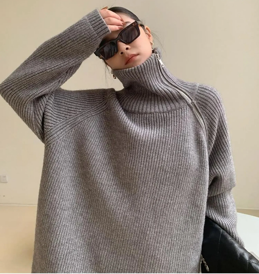 Person wearing a gray sweater and sunglasses against a plain background