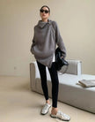 Woman wearing a gray sweater and black leggings in a minimalistic room.