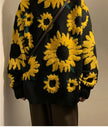 Black sweater with yellow sunflower patterns worn by a person against a neutral background