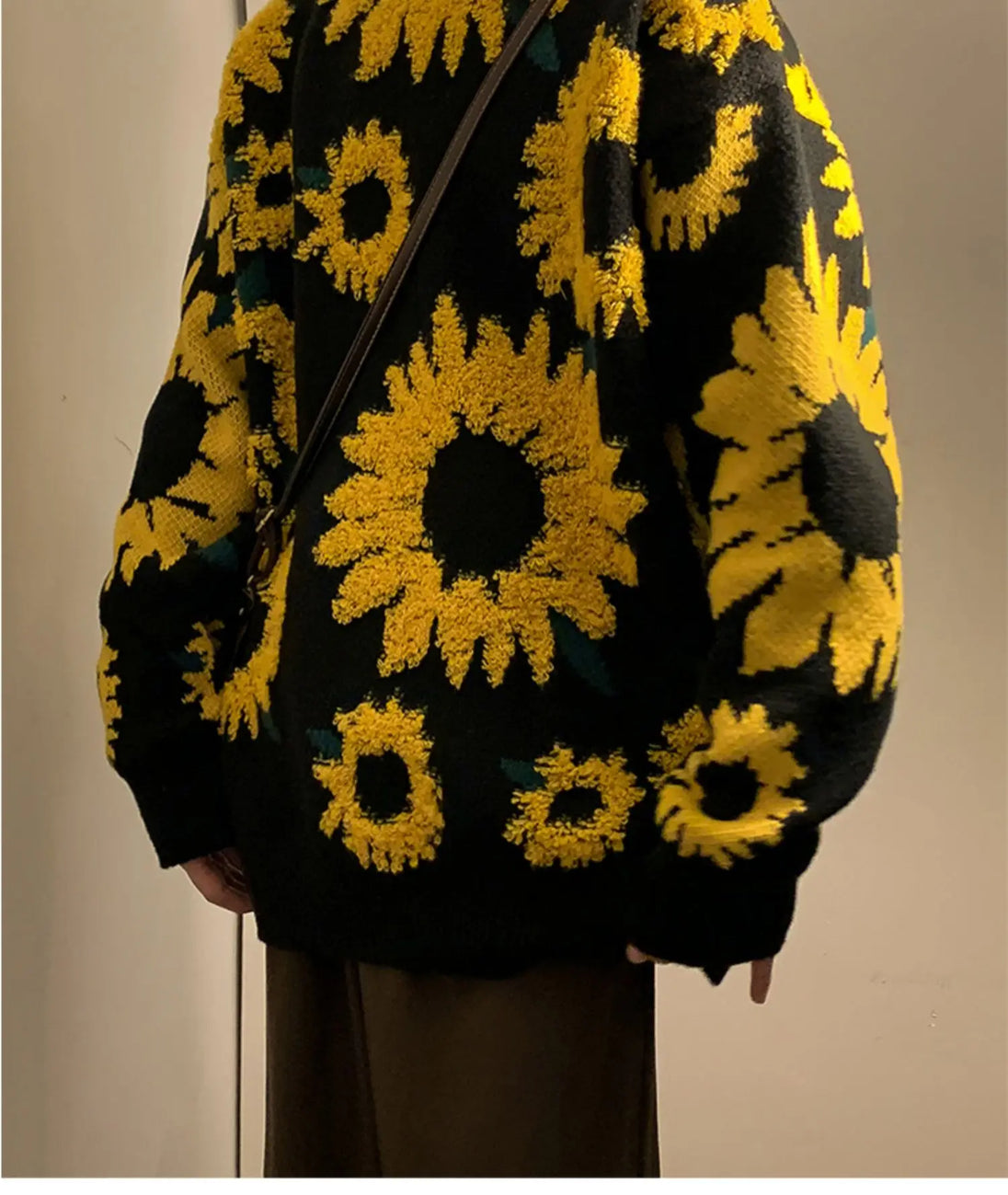 Black sweater with yellow sunflower patterns worn by a person against a neutral background