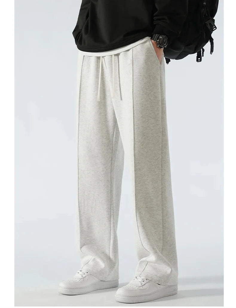 Person wearing light gray sweatpants with a black top and white sneakers on a white background